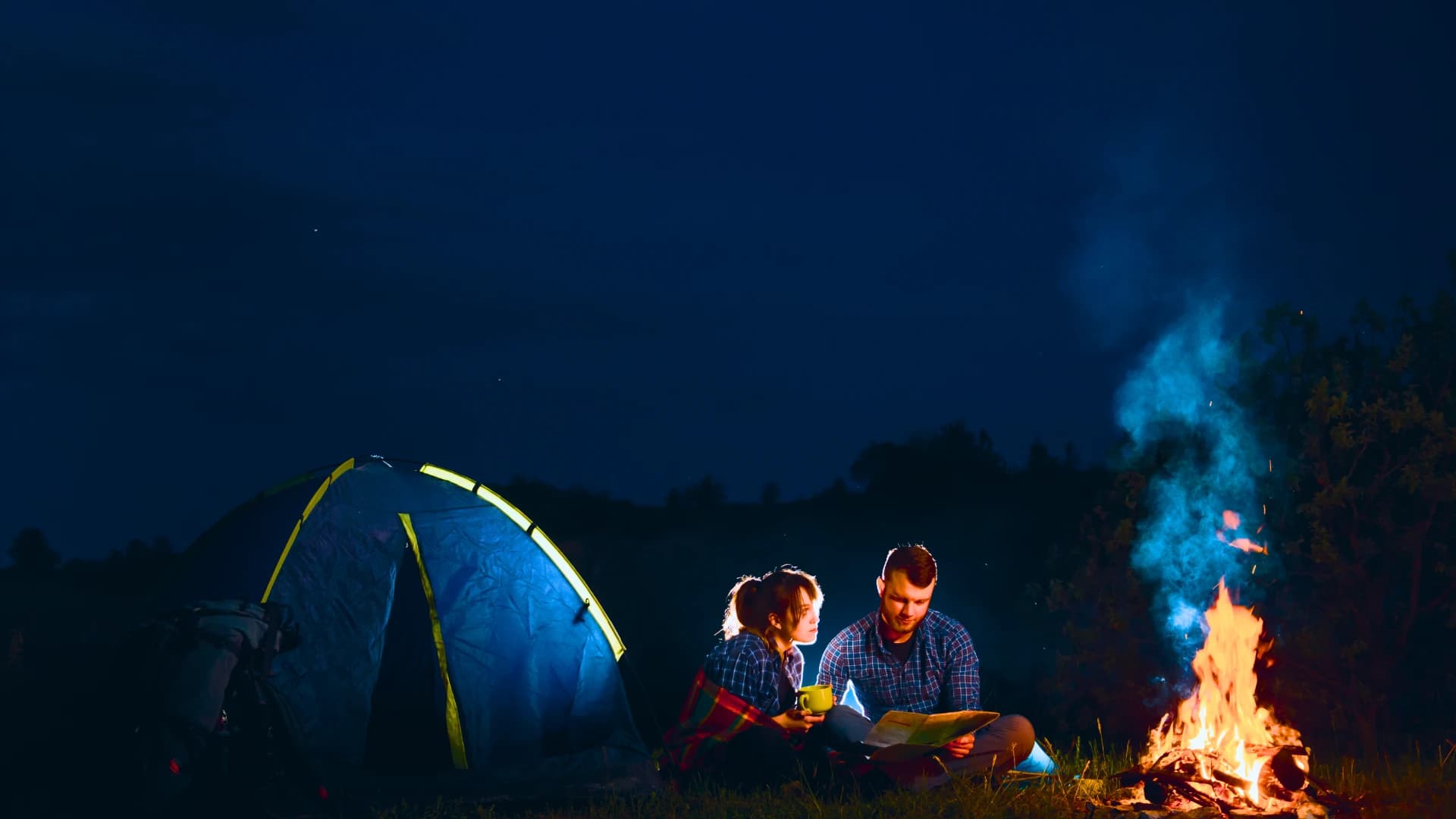 A couple reading a map together by a campfire at night.