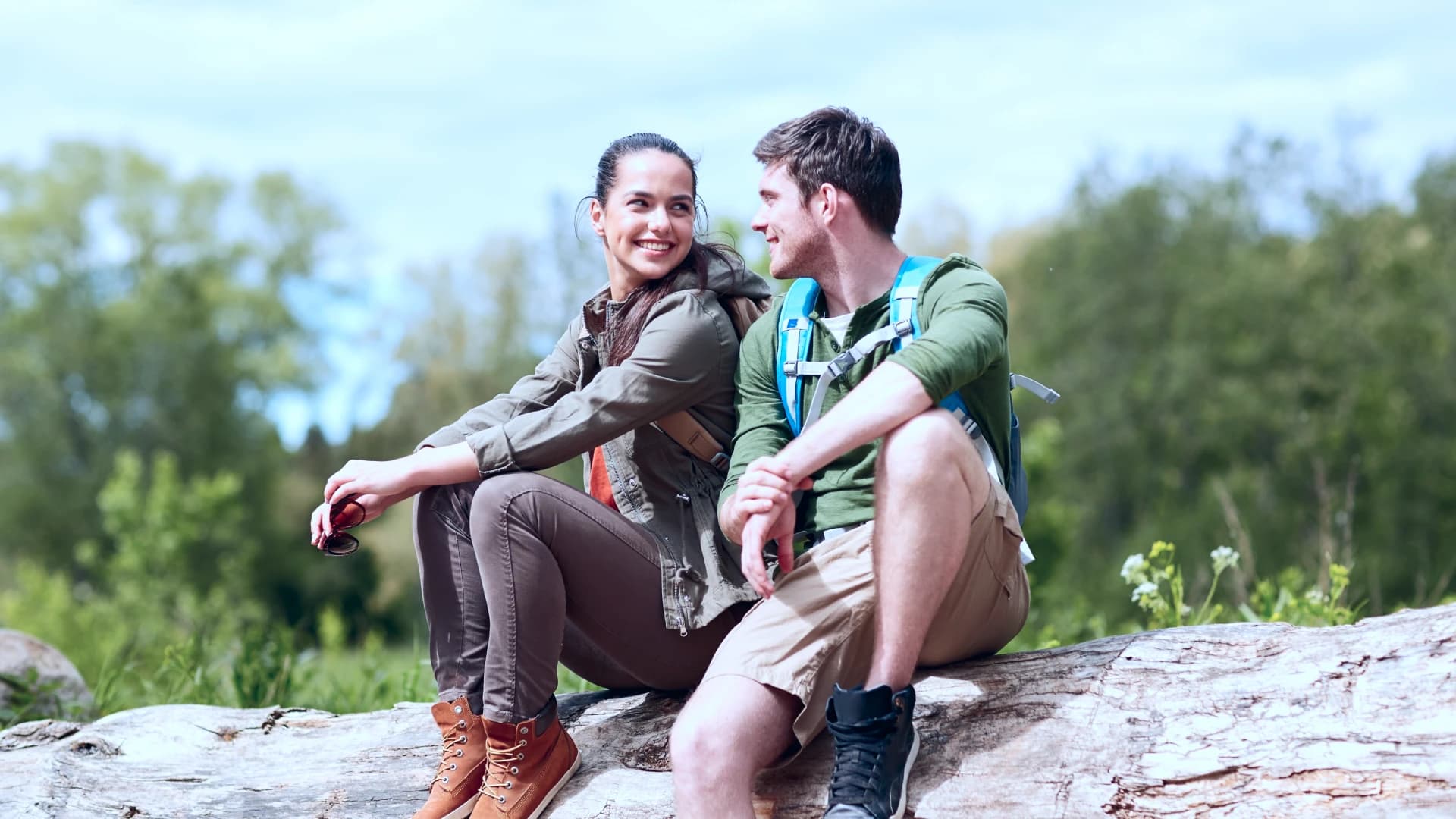 Two hikers sitting together on a fallen log, smiling.